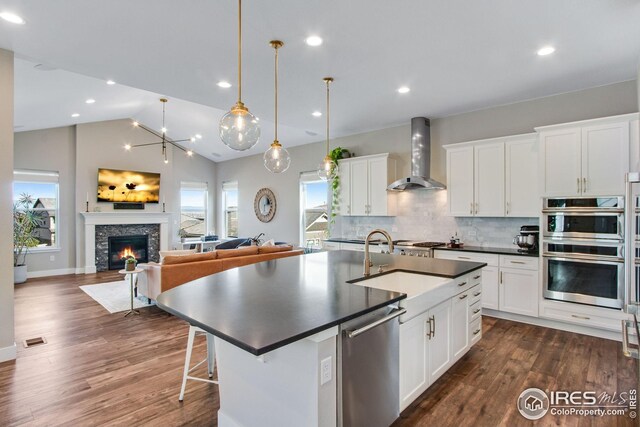 16335 Spanish Peak Way, Broomfield, CO 80023 - kitchen featuring dark countertops, a sink, open floor plan, wall chimney exhaust hood, and appliances with stainless steel finishes