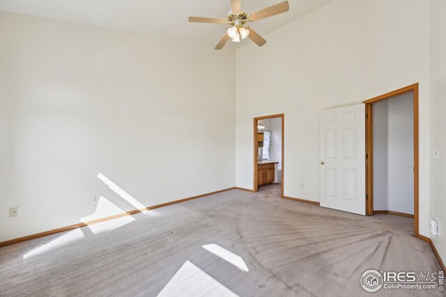 unfurnished bedroom featuring high vaulted ceiling, light carpet, baseboards, and ensuite bathroom