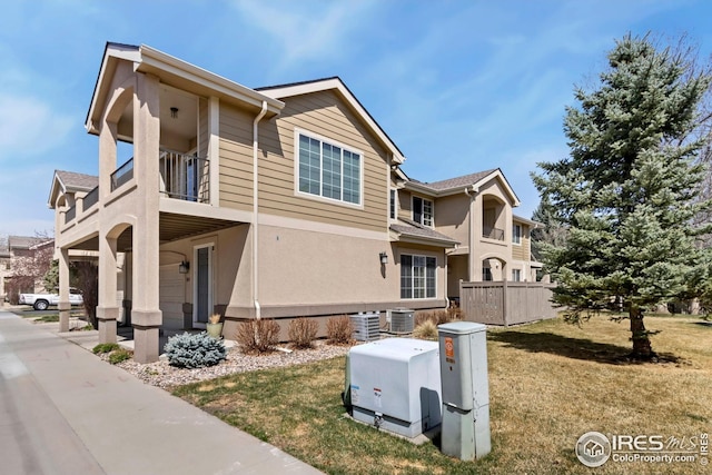 view of side of home featuring a lawn, a balcony, cooling unit, and stucco siding