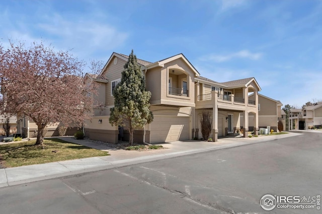 view of front of home with an attached garage, concrete driveway, stucco siding, and a balcony