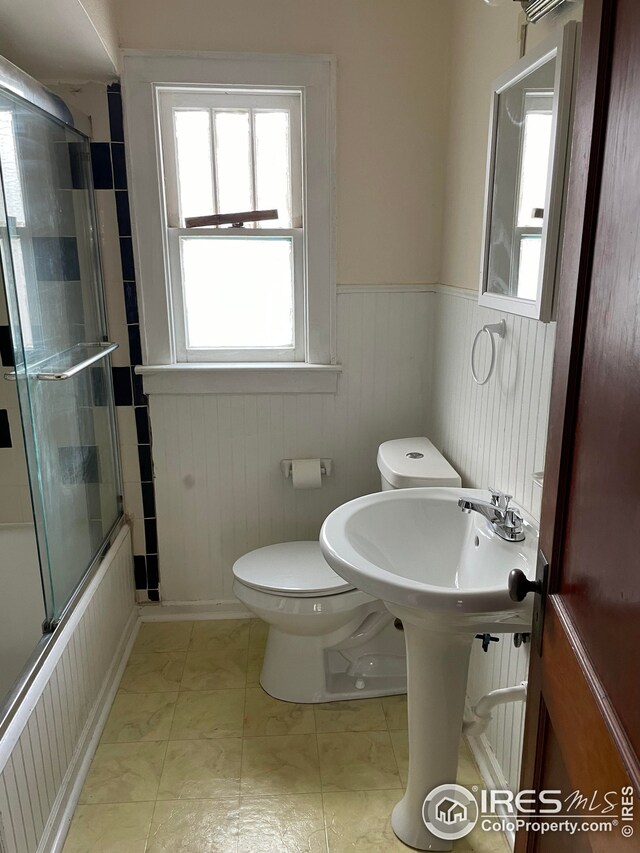 bathroom with enclosed tub / shower combo, toilet, and a wainscoted wall