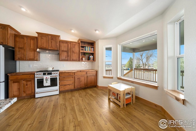 kitchen featuring freestanding refrigerator, white gas stove, backsplash, brown cabinetry, and under cabinet range hood