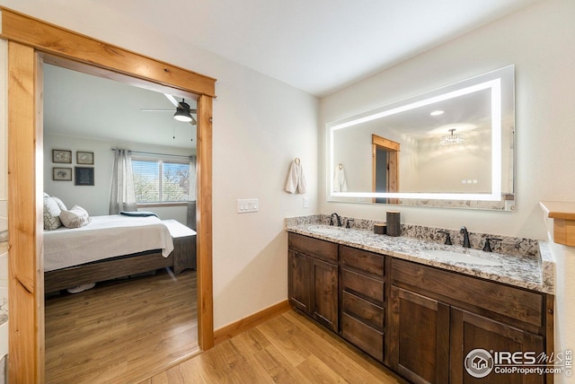 bathroom featuring double vanity, wood finished floors, connected bathroom, a sink, and baseboards
