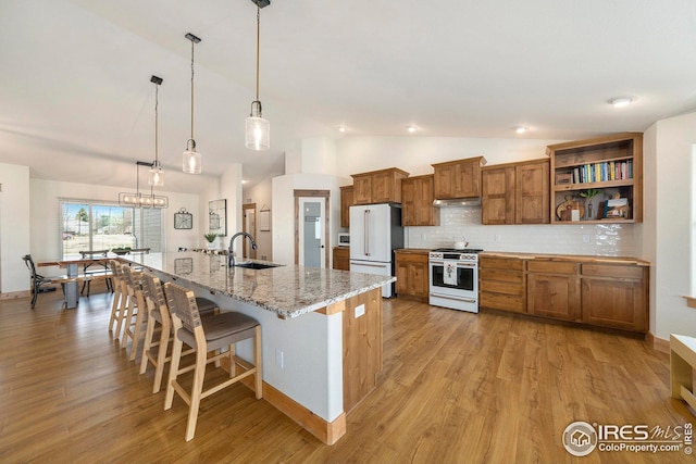 kitchen with brown cabinets, vaulted ceiling, a sink, stainless steel range with gas cooktop, and freestanding refrigerator