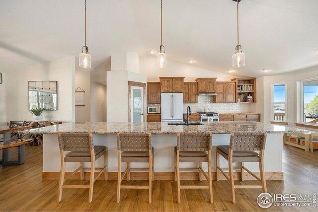 kitchen featuring a sink, lofted ceiling, open shelves, brown cabinetry, and under cabinet range hood