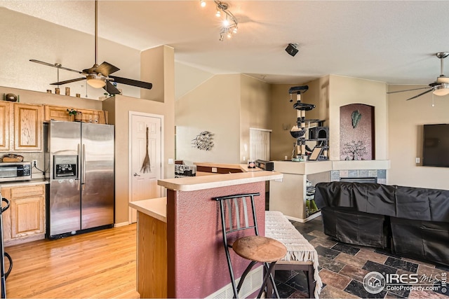 kitchen featuring open floor plan, appliances with stainless steel finishes, ceiling fan, light countertops, and a breakfast bar area