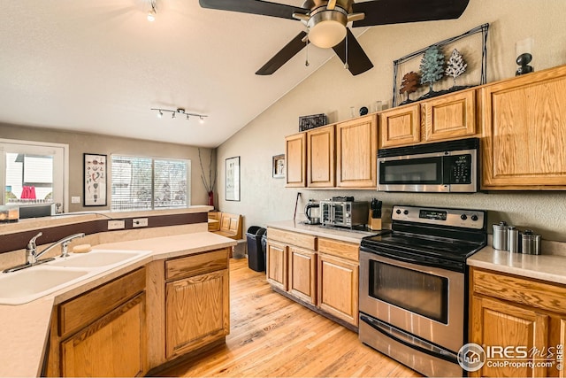 kitchen featuring a sink, light wood-style floors, light countertops, lofted ceiling, and appliances with stainless steel finishes