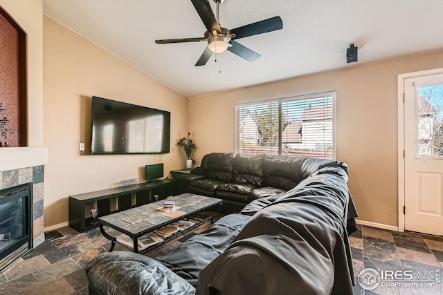 living area with a ceiling fan, baseboards, stone tile floors, and a tile fireplace