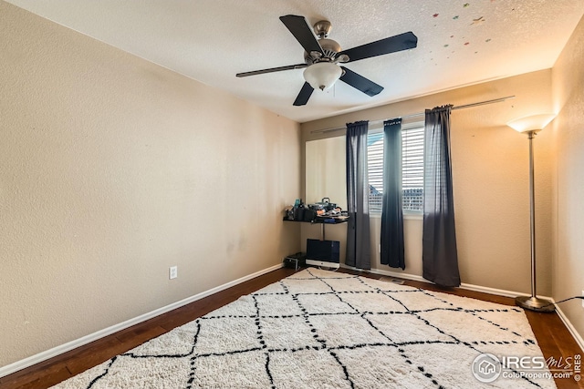 empty room with wood finished floors, a ceiling fan, baseboards, and a textured wall