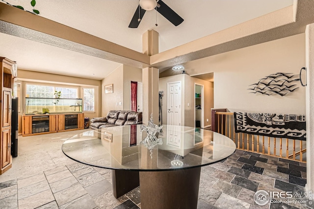 dining space featuring stone tile floors, lofted ceiling, beverage cooler, and ceiling fan