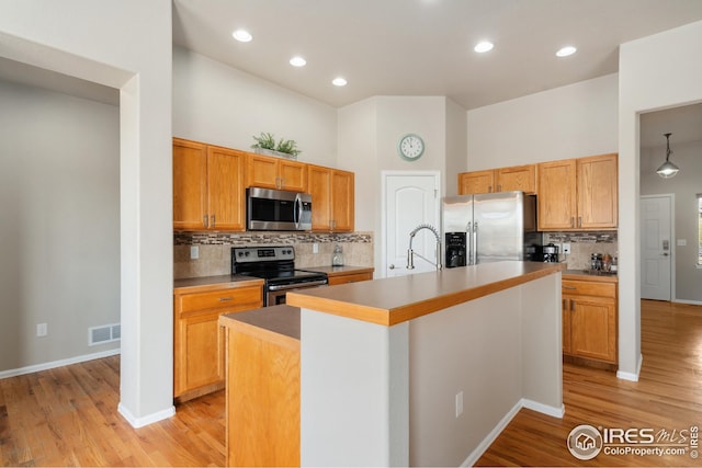 kitchen featuring an island with sink, stainless steel appliances, backsplash, visible vents, and light wood-type flooring