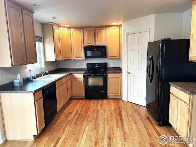 kitchen featuring dark countertops, a sink, black appliances, light wood-style flooring, and recessed lighting