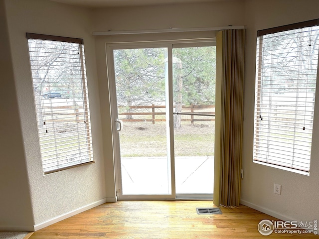 doorway featuring baseboards, a textured wall, light wood-style floors, and visible vents