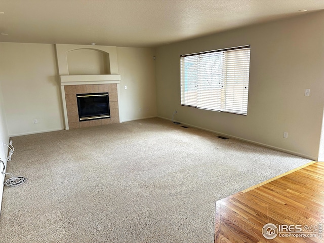 unfurnished living room featuring a tile fireplace, visible vents, baseboards, and carpet