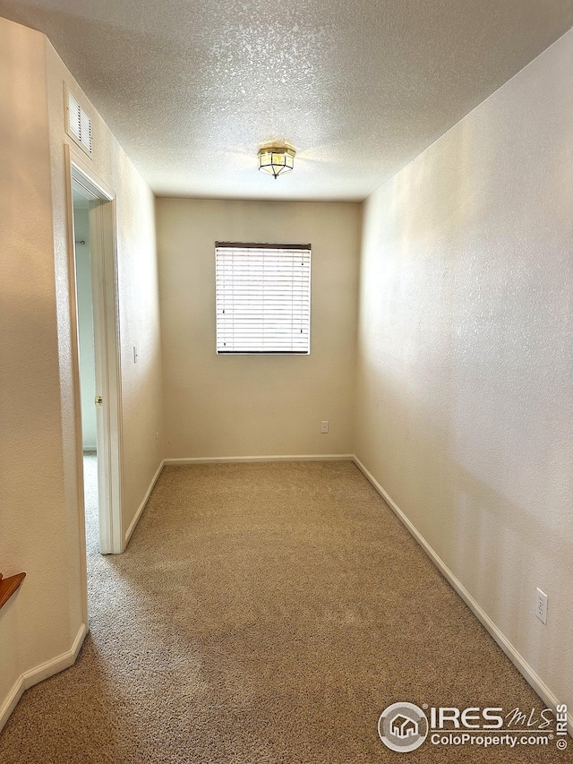 carpeted spare room with baseboards, visible vents, and a textured ceiling