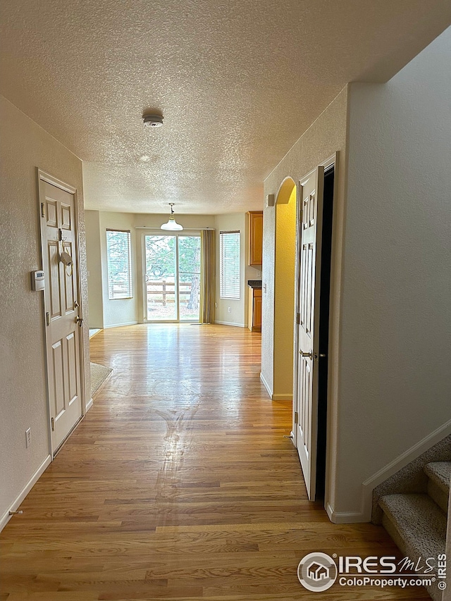interior space with arched walkways, light wood-style floors, a textured wall, and a textured ceiling