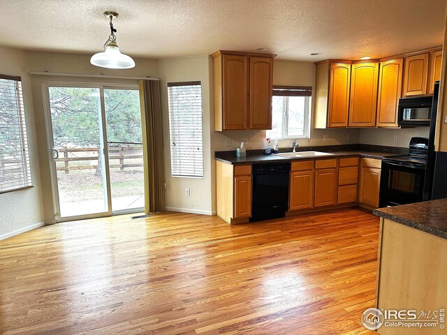 kitchen with a sink, a textured ceiling, light wood-type flooring, dark countertops, and black appliances