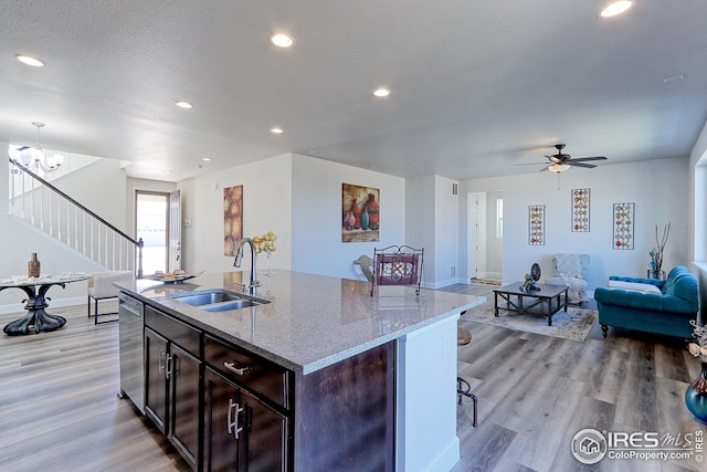 kitchen featuring stainless steel dishwasher, a sink, open floor plan, light wood finished floors, and recessed lighting