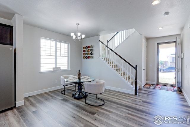 dining area with baseboards, wood finished floors, a notable chandelier, and stairway