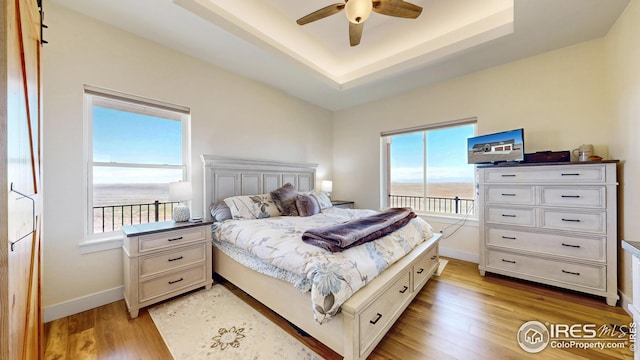 bedroom featuring a raised ceiling, light wood-style floors, baseboards, and ceiling fan