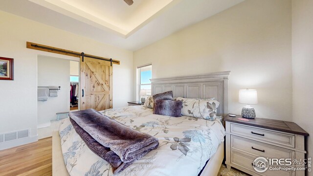bedroom featuring a barn door, a spacious closet, visible vents, light wood-type flooring, and a closet