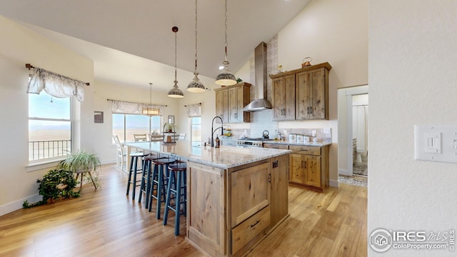 kitchen featuring wall chimney exhaust hood, brown cabinetry, a breakfast bar, and high vaulted ceiling