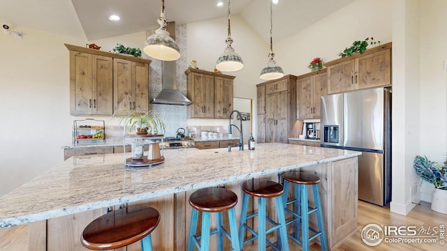 kitchen featuring high vaulted ceiling, a spacious island, stainless steel appliances, light wood-style flooring, and wall chimney exhaust hood