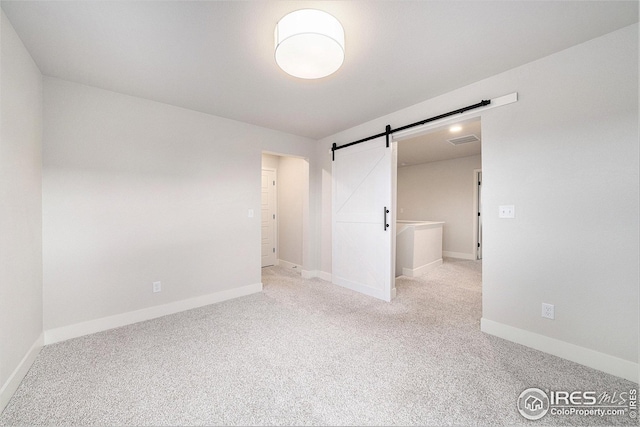 spare room featuring light carpet, baseboards, visible vents, and a barn door
