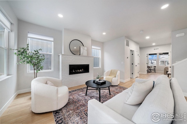 living room featuring a healthy amount of sunlight, a glass covered fireplace, light wood finished floors, and recessed lighting