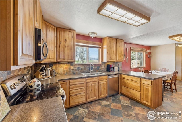 kitchen featuring appliances with stainless steel finishes, a sink, a peninsula, a textured ceiling, and tasteful backsplash
