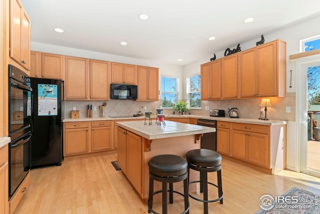 kitchen with a breakfast bar, light wood-style floors, a center island, decorative backsplash, and black appliances
