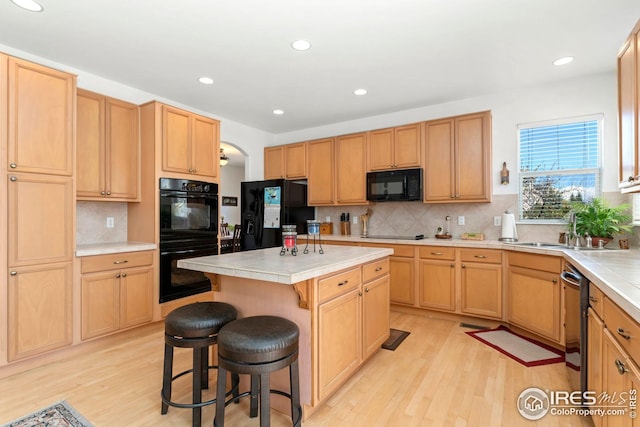 kitchen with black appliances, tile counters, a sink, and light wood-style flooring