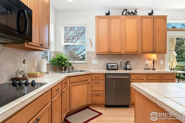 kitchen with light wood-style flooring, tile countertops, a sink, and black appliances