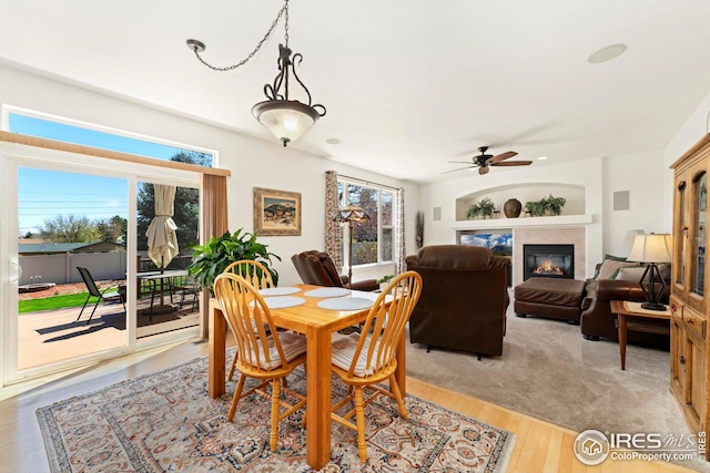 dining area with ceiling fan, a glass covered fireplace, and light wood-style flooring