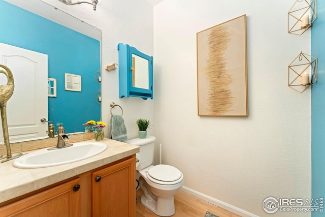 half bathroom featuring baseboards, wood finished floors, vanity, and toilet