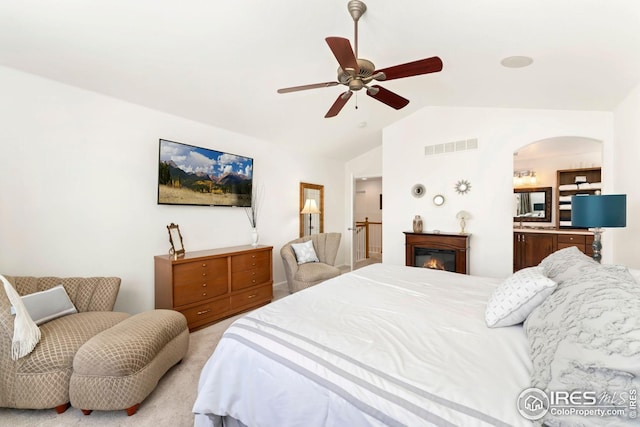 bedroom with vaulted ceiling, visible vents, a ceiling fan, a glass covered fireplace, and light colored carpet