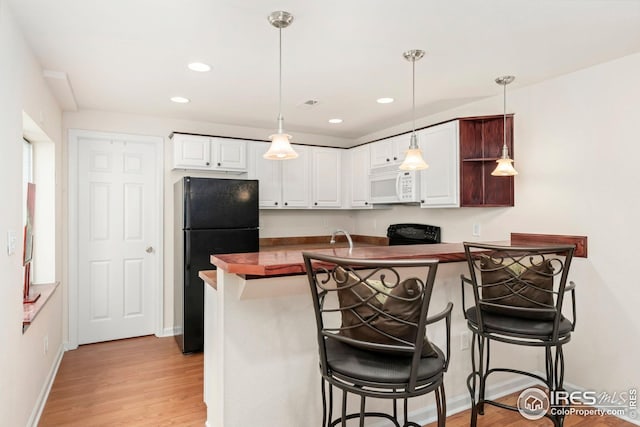 kitchen with dark countertops, black appliances, light wood-style flooring, a breakfast bar area, and white cabinetry