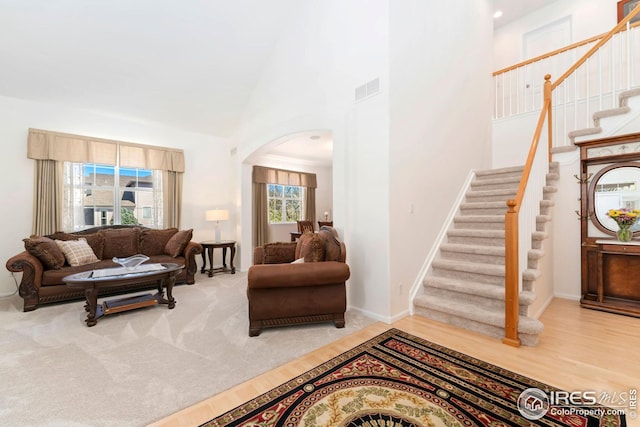 living room with arched walkways, visible vents, baseboards, a towering ceiling, and stairway