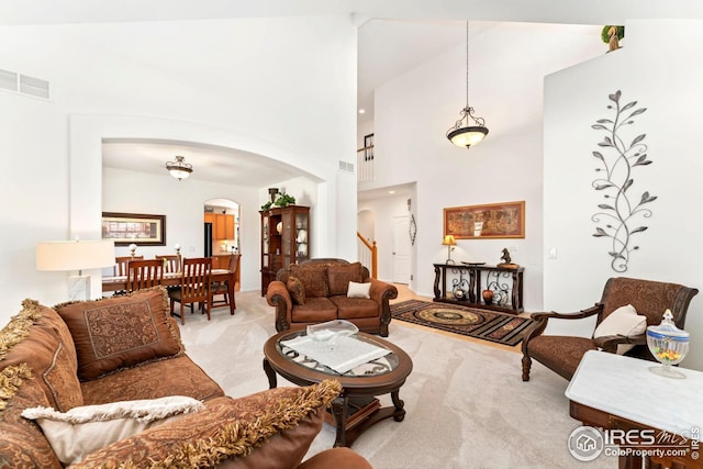 living area with a high ceiling, arched walkways, carpet flooring, and visible vents