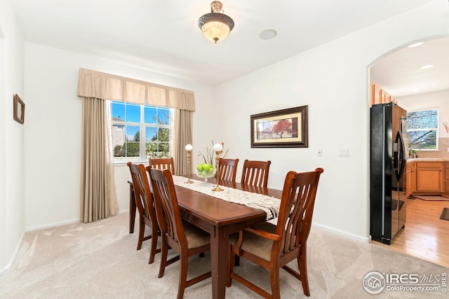 dining space with arched walkways, baseboards, and light carpet