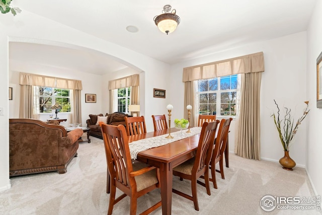 dining area with arched walkways, light carpet, and baseboards