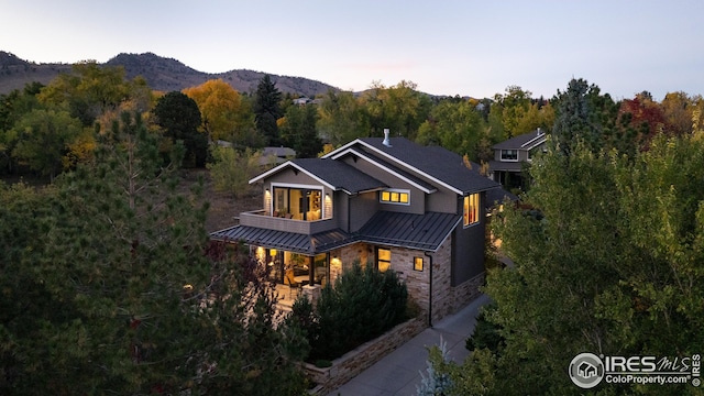 view of front facade featuring a standing seam roof, stone siding, a view of trees, a mountain view, and metal roof