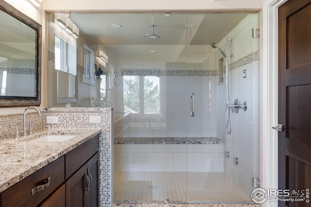 full bath featuring decorative backsplash, vanity, and a stall shower