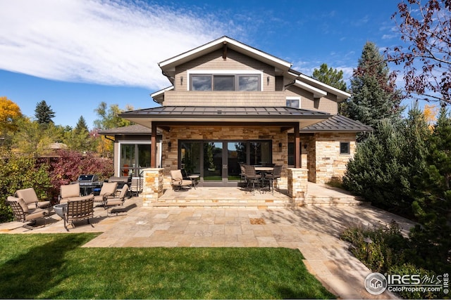 rear view of house featuring a standing seam roof, stone siding, metal roof, a patio area, and an outdoor hangout area