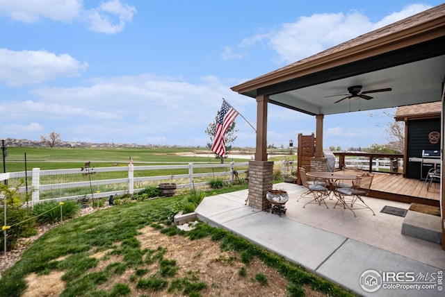 view of patio featuring a rural view, outdoor dining area, fence, a wooden deck, and ceiling fan