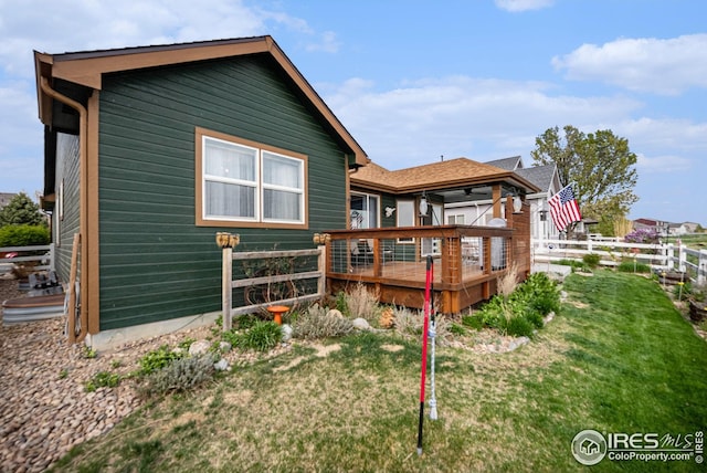 rear view of property featuring a wooden deck, a lawn, and fence