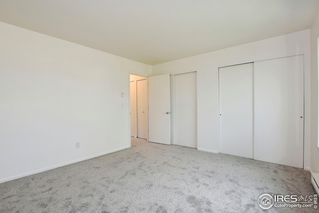 unfurnished bedroom with two closets, carpet floors, and baseboards