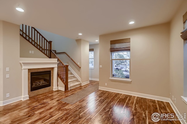unfurnished living room with recessed lighting, stairway, wood finished floors, baseboards, and a tiled fireplace