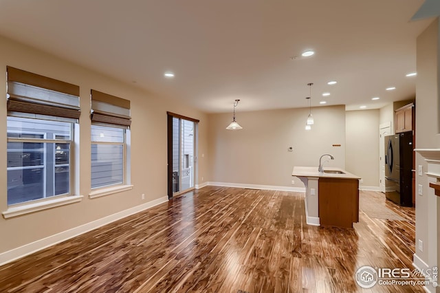 kitchen featuring hanging light fixtures, a sink, an island with sink, dark wood-style floors, and freestanding refrigerator