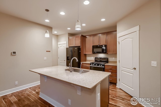 kitchen featuring wood finished floors, a sink, black appliances, a kitchen island with sink, and a breakfast bar
